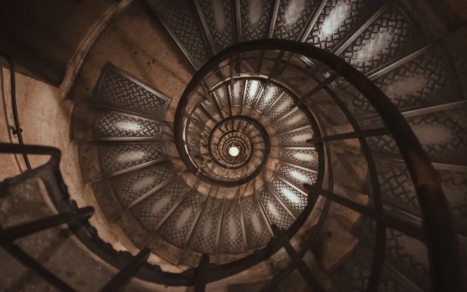 Un escalier en colimaçon vu d’en haut, dans une lumière chaude